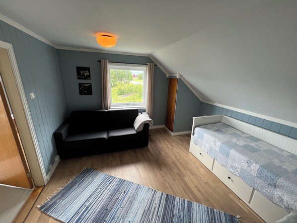 A small, cozy room with a black sofa, a single bed, a window with a view of greenery, and a ceiling light. - Fabulous 4-bedroom villa with AC in Møre og Romsdal, boat available (Møre og Romsdal)