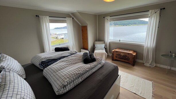 A bedroom with a large bed, a wooden bench, a small table, and a view of a body of water. - Fabulous 4-bedroom villa with AC in Møre og Romsdal, boat available (Møre og Romsdal)