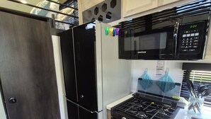 Una cucina con un frigorifero nero, un fornello, un forno a microonde ed elementi pensili in legno.