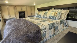 Una camera da letto con un letto, un pouf importante, una testiera e una TV integrata.