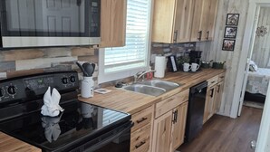 A modern kitchen with wooden cabinets, a black stove, and a microwave. - Sunrise Haven Tiny Home (Big Cabin)