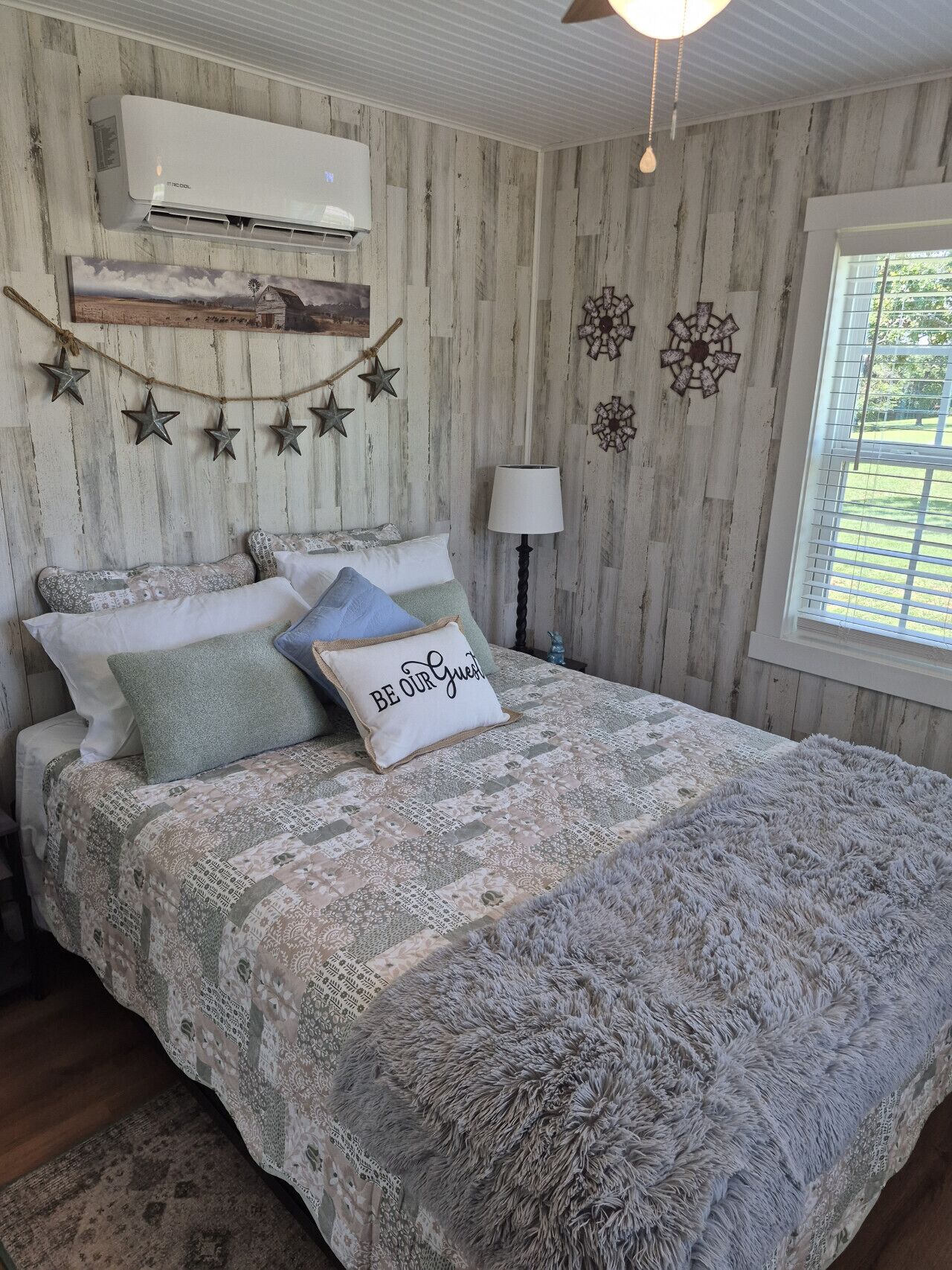 Een slaapkamer met een bed, decoratieve wanddecoraties, een lamp en een raam met uitzicht.