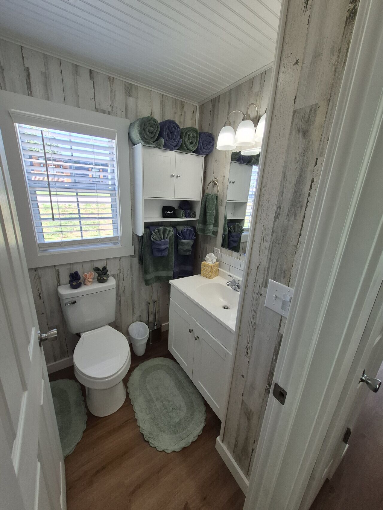 Une salle de bain avec des toilettes, un lavabo et une fenêtre avec des stores.