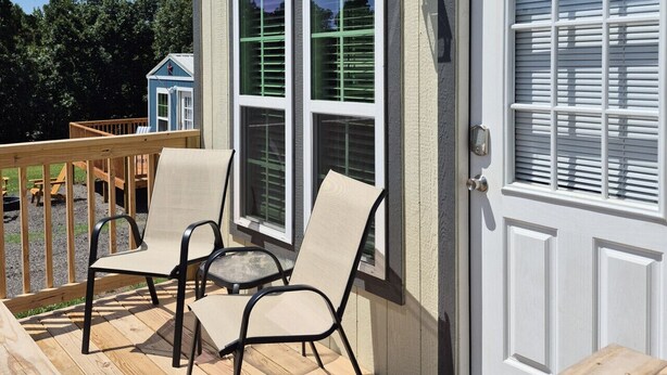 A deck with outdoor furniture, a door with a window, and a small window above the door. - Sunrise Haven Tiny Home (Big Cabin)