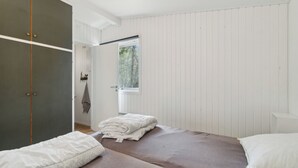 A bedroom with two beds, a wardrobe, and a window with a view of trees.