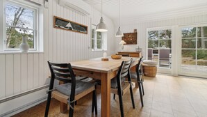 A dining area with a wooden table and chairs, pendant lights, a white-framed window, and a view of the outdoors.