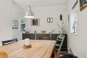 A dining area with a wooden table, a pendant light, and a view of the kitchen.