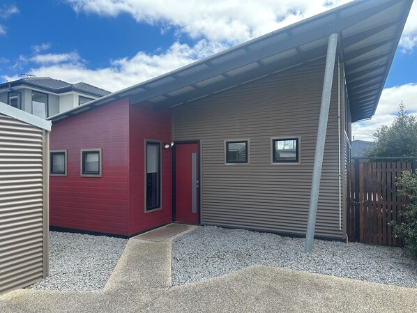 Une maison moderne avec une façade rouge et beige, un porche abrité et une allée gravillonnée.