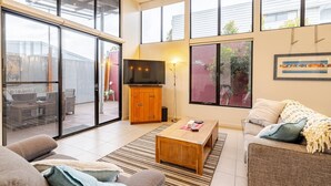 A spacious living room with a large sliding glass door leading to an outdoor area, a wooden coffee table, a sofa, and a television.