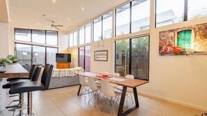 A modern kitchen with a dining area, large windows, and a ceiling fan.