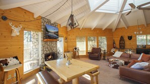 Ein gemütliches Blockhaus-Interieur mit Kamin aus Stein, Holzwänden, einem Esstisch und einer Ledersofa.