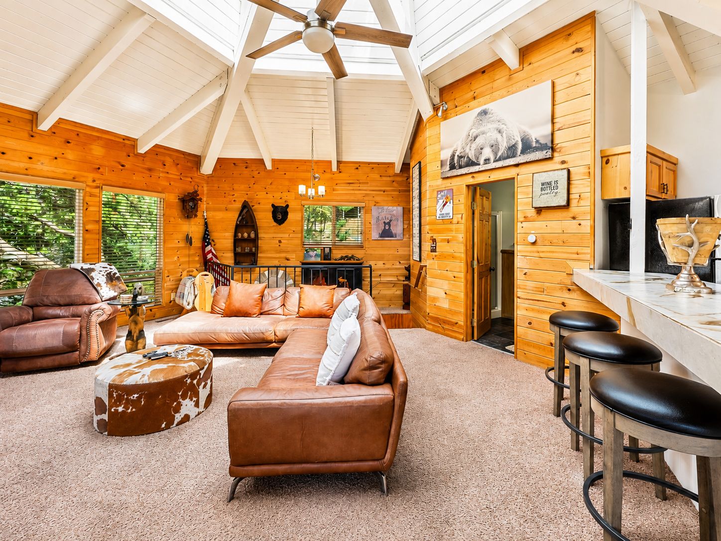 A cozy cabin interior with a leather sofa, a wooden bar area, and a ceiling fan.