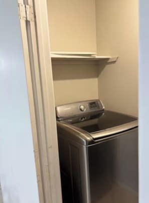 Een kleine wasruimte met een voorlader wasmachine en droger, een witte deur en een beige wand.