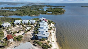 Vista aérea de um hotel costeiro com vários edifícios ao longo da praia, rodeado por florestas de mangue e uma grande extensão de água.