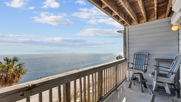 Um deck de madeira com duas cadeiras Adirondack com vista para uma praia e o oceano.