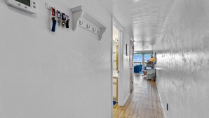 Um corredor com paredes brancas, piso de madeira e porta que dá para um quarto com vista.
