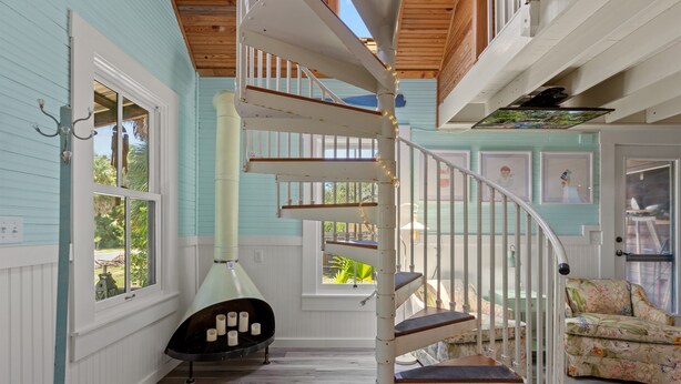 A spiral staircase in a room with wooden floors, a fireplace, and a window overlooking greenery.