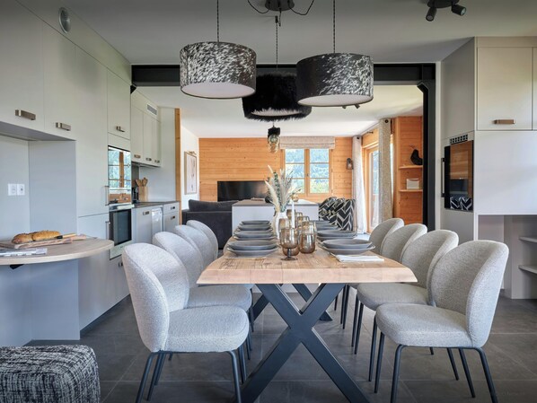 A modern kitchen with white cabinets, a wooden dining table, and grey upholstered chairs.