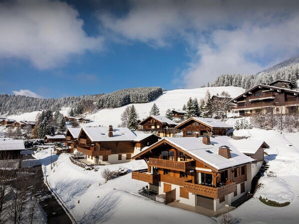 Une station de montagne enneigée, avec des chalets en bois et une piste de ski en arrière-plan.