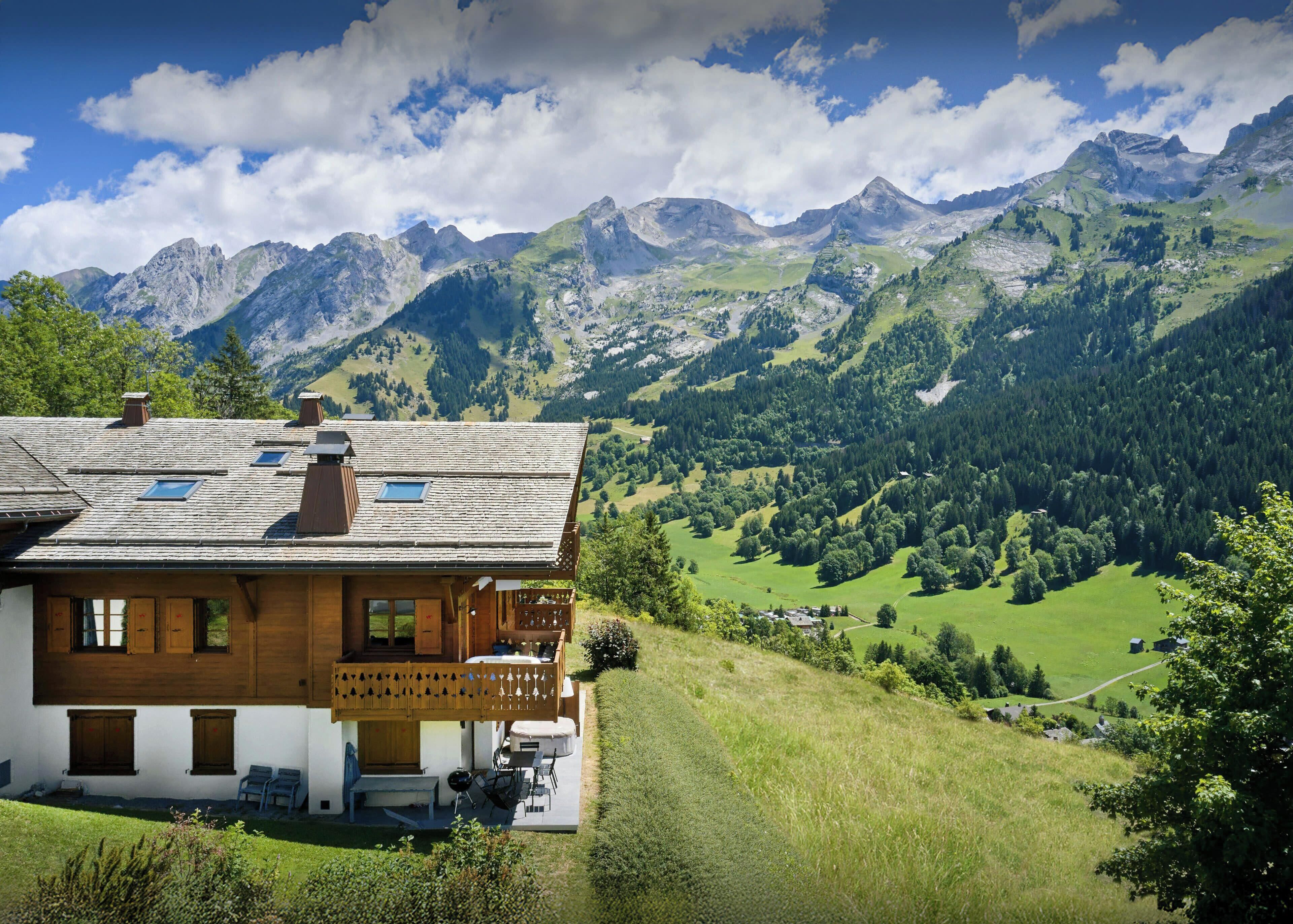 A chalet with a balcony, wooden exterior, and a view of a mountainous landscape.