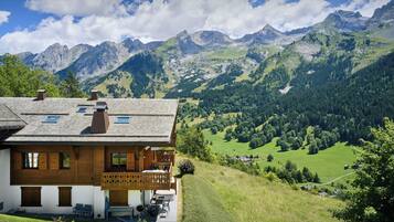 A chalet with a balcony, wooden exterior, and a view of a mountainous landscape.