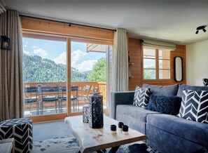 Una sala de estar moderna con un sofá, una mesa de centro y vistas a un paisaje montañoso a través de amplios ventanales correderas.