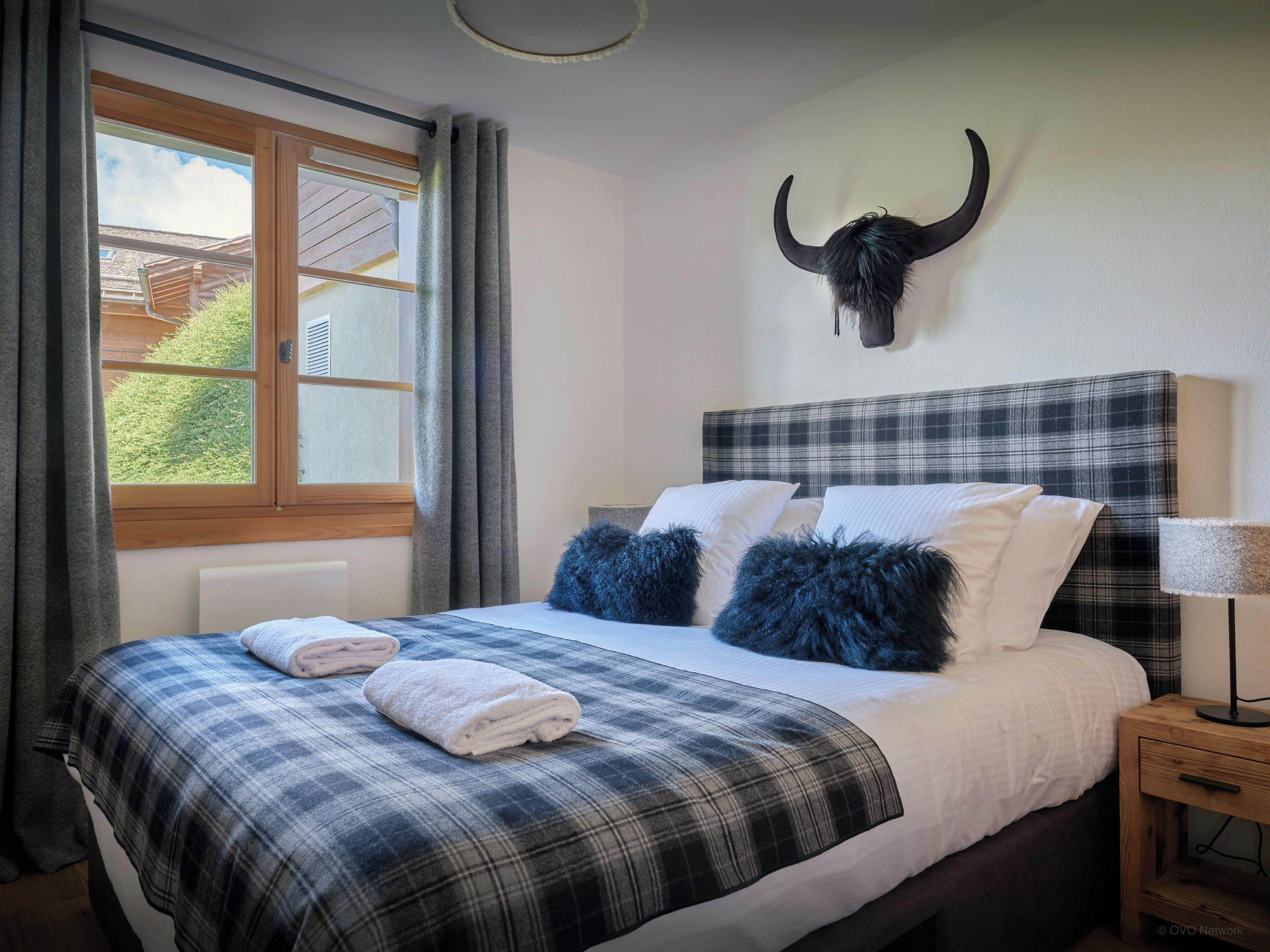 A bedroom with a bed, pillows, a lamp, a window, and a bull skull decoration.