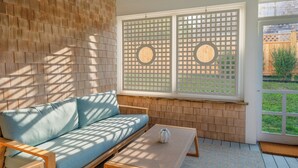 A room with a wooden wall, a blue sofa, a small table with a vase, and a window with a lattice screen.