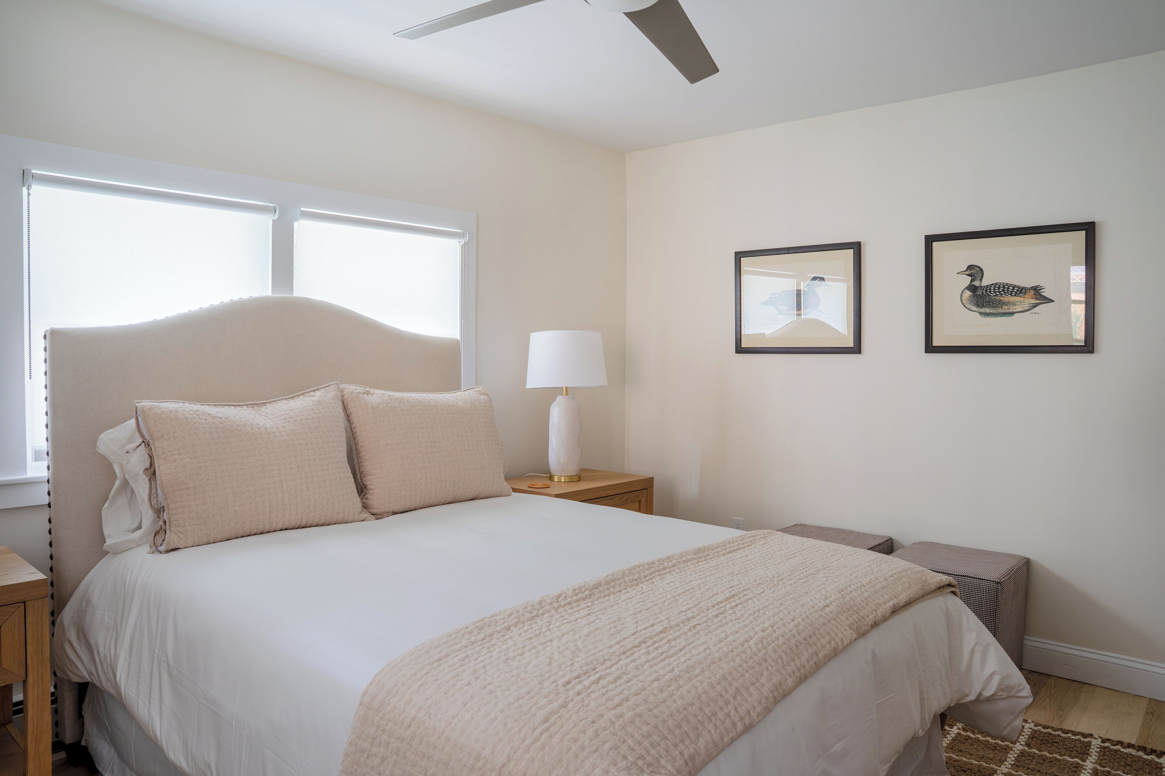 Een slaapkamer met een bed, nachtkastje, lamp en twee foto's in lijsten aan de muur.
