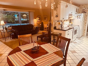 Un comedor con una mesa dispuesta para cuatro, una cocina con armarios blancos y vistas al exterior a través de un amplio ventanal.