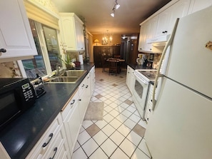 Una cocina con armarios blancos, encimera negra, microondas, estufa y refrigerador.