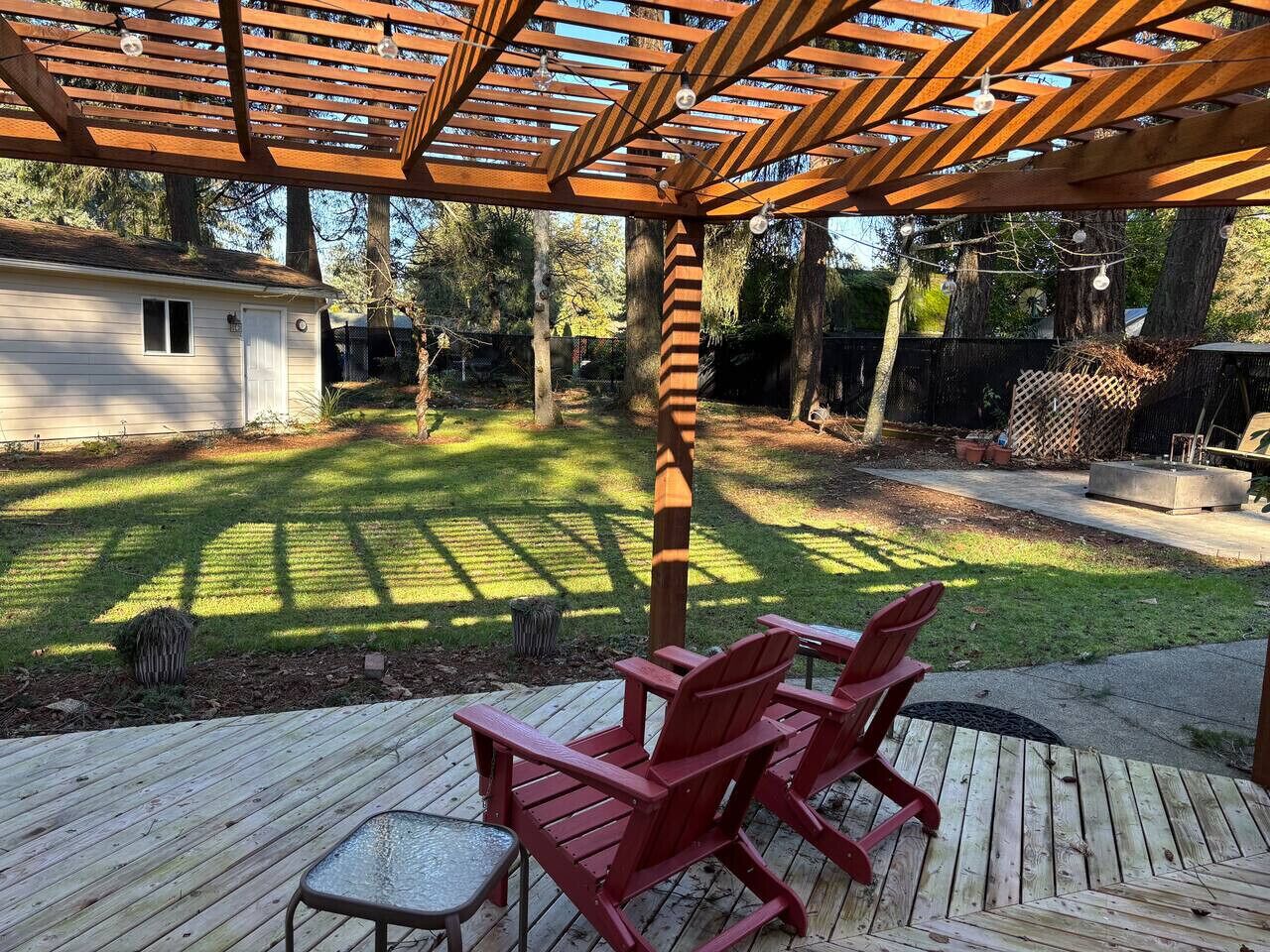 Een houten terras met rode stoelen, een pergola en een verzorgd gazon.