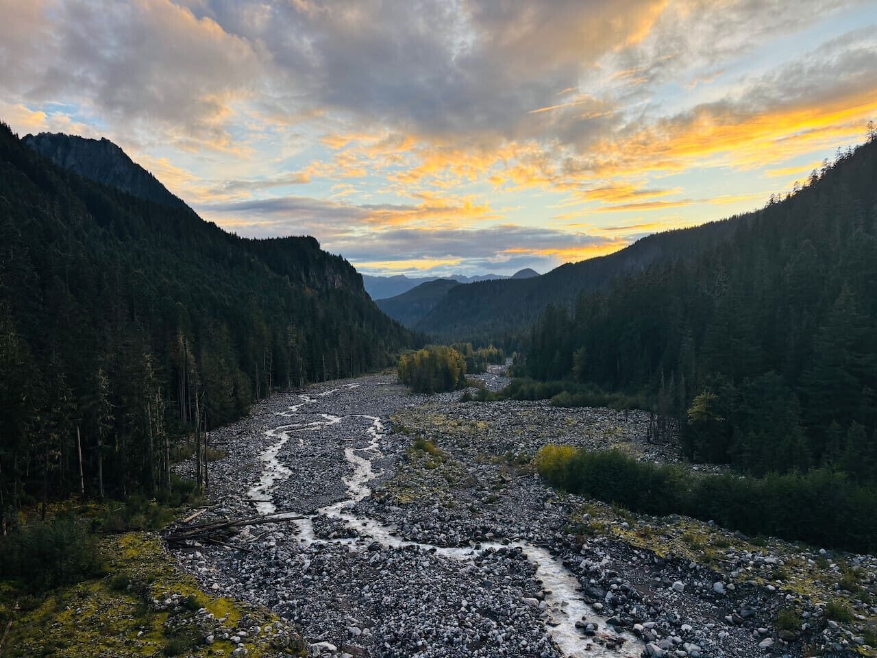 Une rivière qui traverse une vallée boisée, avec des montagnes en arrière-plan.