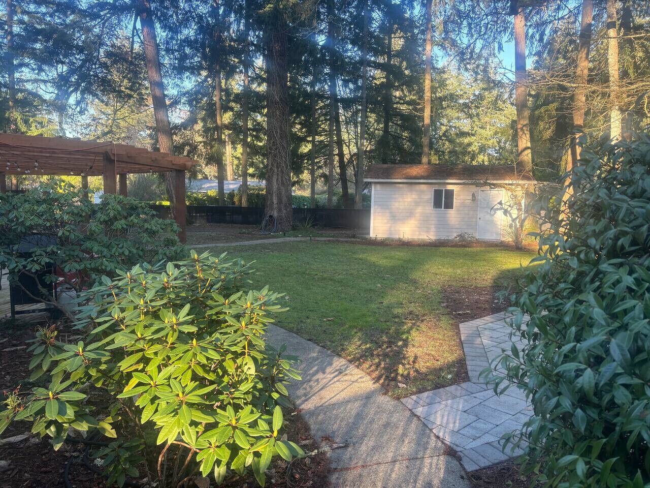 Un jardin avec un petit abri de jardin, une pergola en bois et une pelouse bien entretenue.