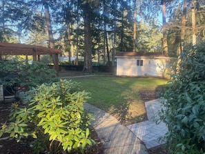 Un patio trasero con un cobertizo pequeño, una pérgola de madera y un césped bien cuidado.