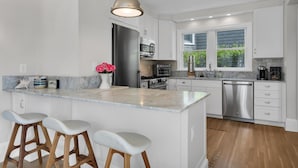 A modern kitchen with white cabinets, a marble countertop, stainless steel appliances, and a central island with bar stools.