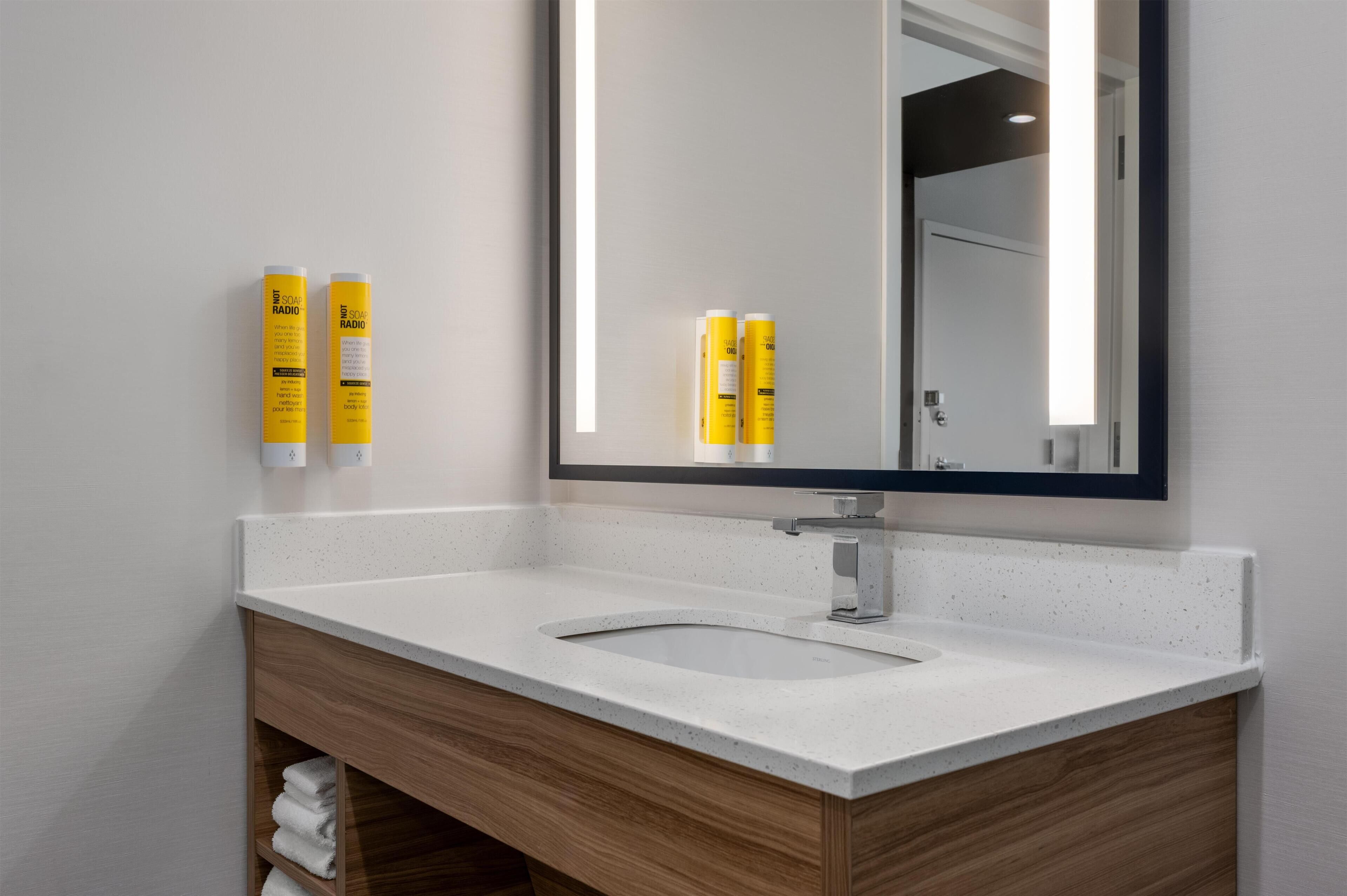 A modern bathroom with a white sink, wooden vanity, and two yellow bottles on the wall.