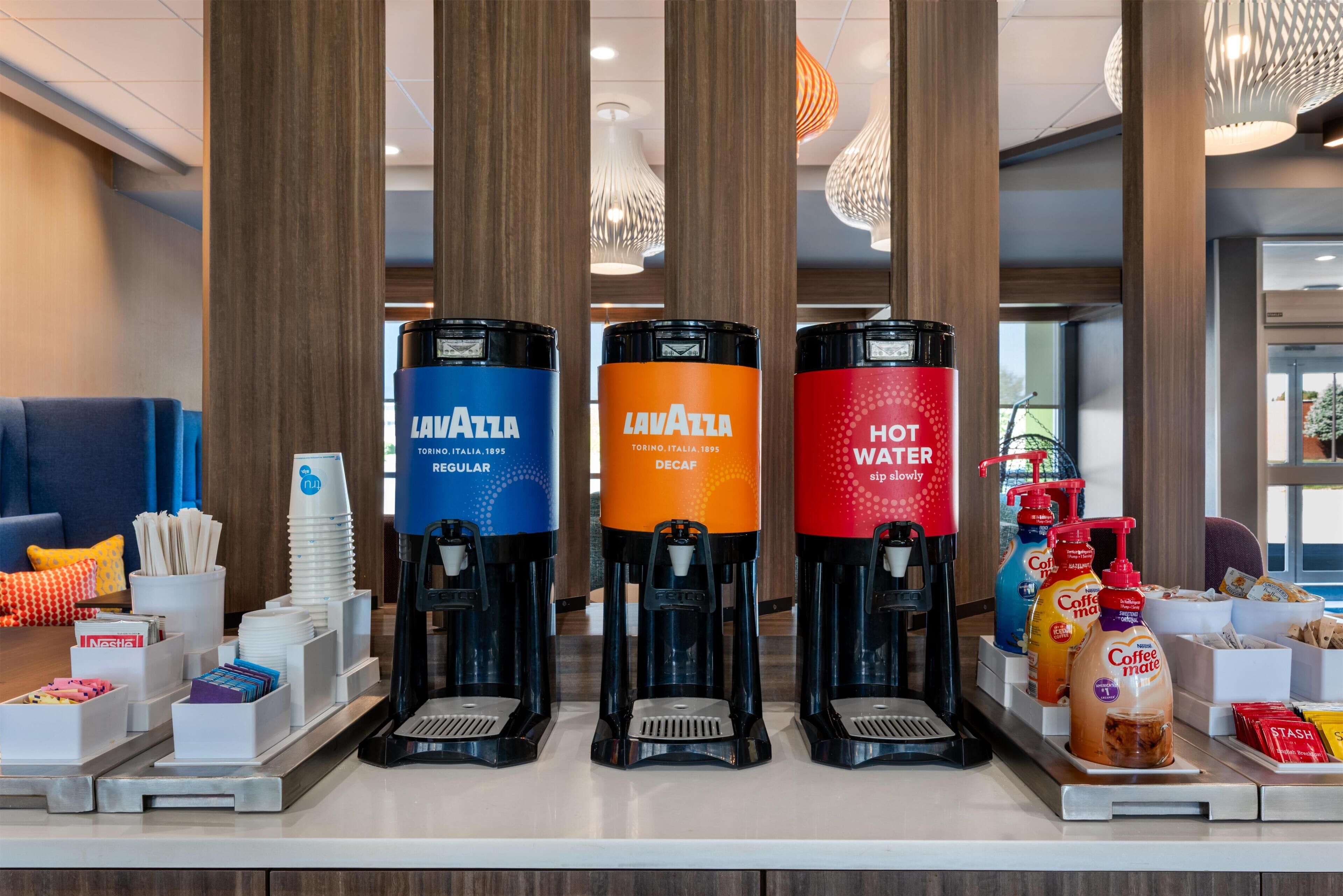 A coffee station with three dispensers labeled 'Lavazza Regular,' 'Lavazza Decaf,' and 'Hot Water.'