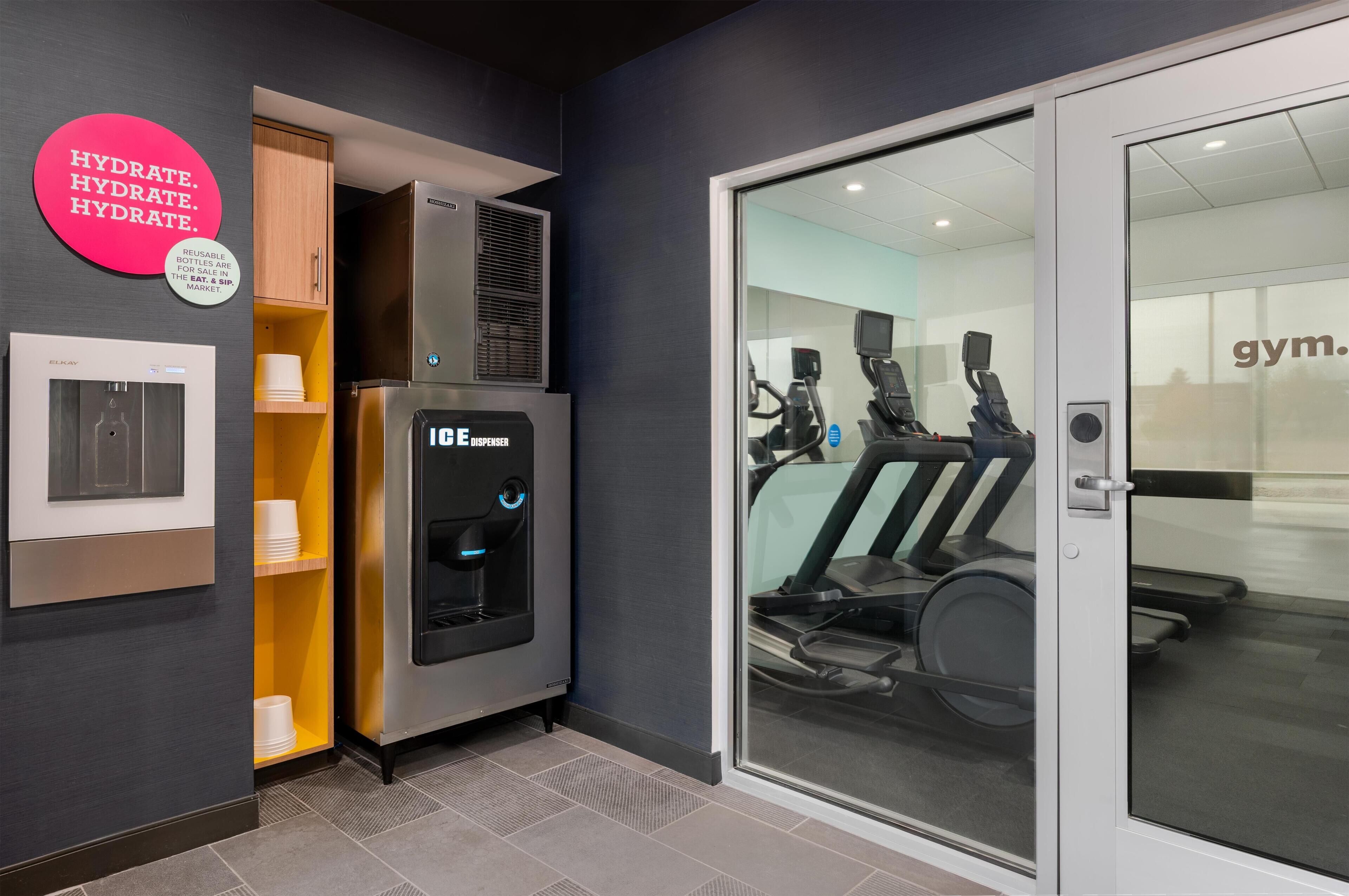 Een fitnessruimte met trainingsapparatuur, een waterdispenser en een bord aan de muur.
