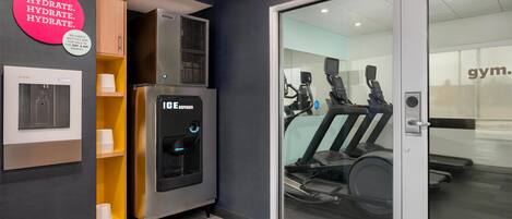 Een fitnessruimte met trainingsapparatuur, een waterdispenser en een bord aan de muur.