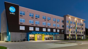 Een modern hotelgebouw met een opvallend 'tru by Hilton' bord, meerdere verdiepingen en een goed verlichte entree.