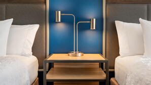Een hotelkamer met twee bedden, een houten nachtkastje en een moderne vloerlamp.