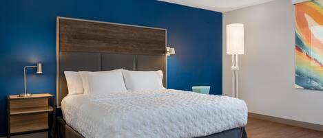 A modern hotel room with a large bed, a nightstand, a bedside lamp, and a colorful abstract painting on the wall.