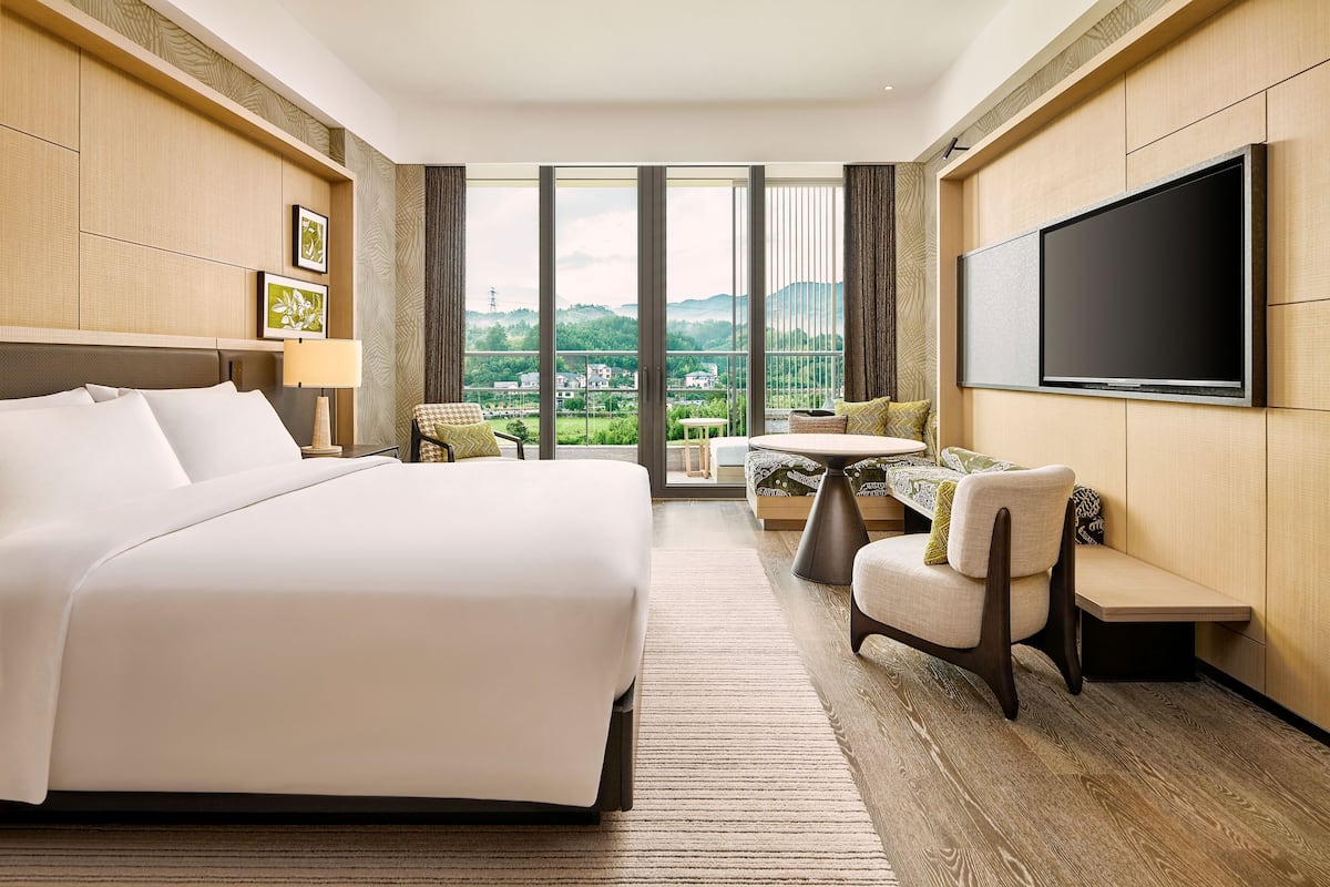 A hotel room with a large bed, a seating area with a table, and a TV mounted on the wall.