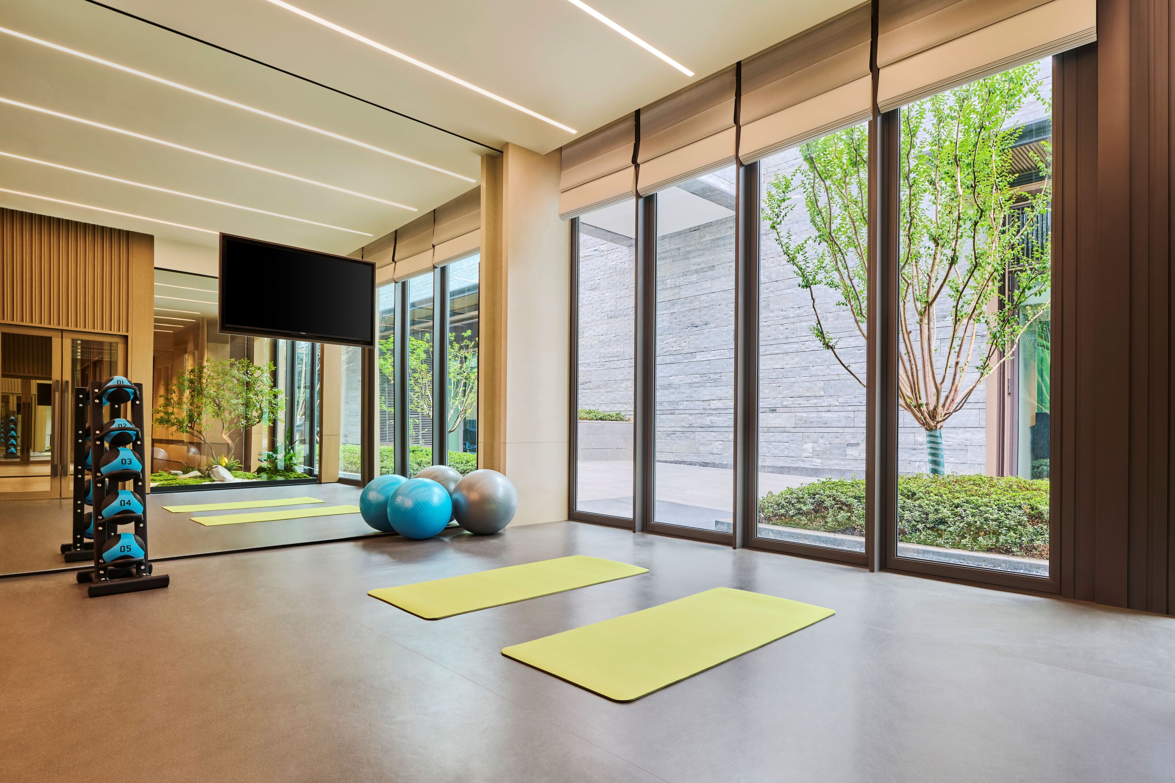 A modern gym with exercise equipment, yoga mats, and large windows offering views of the outdoors.