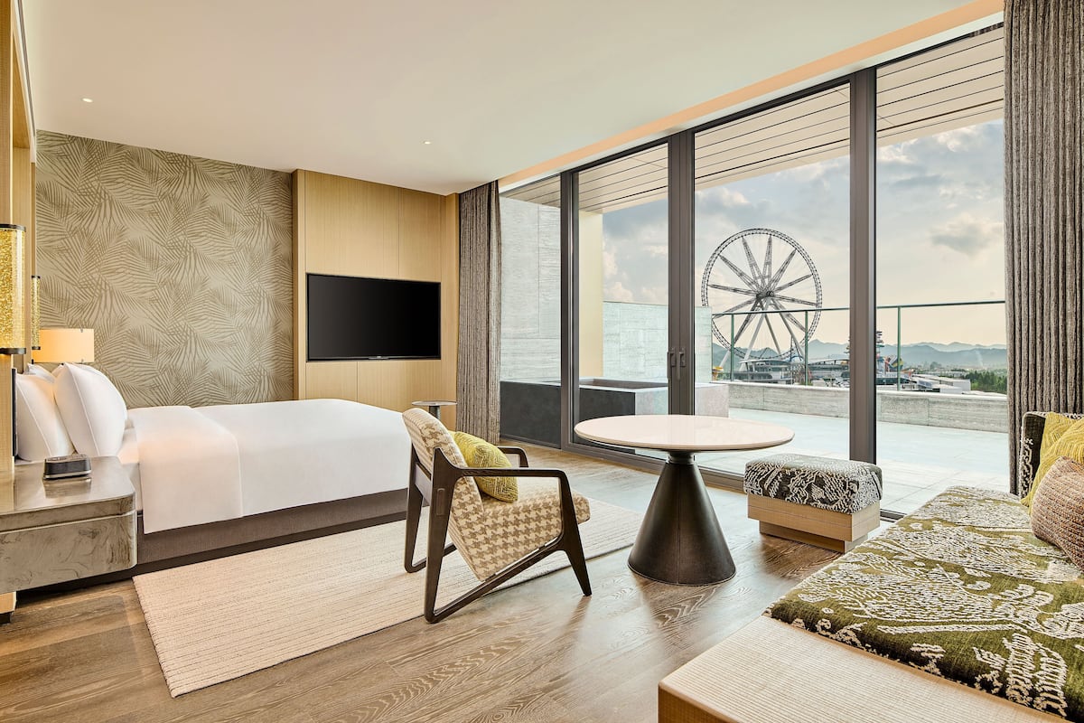 A modern hotel room with a large bed, a TV, a dining table, and a view of a Ferris wheel.