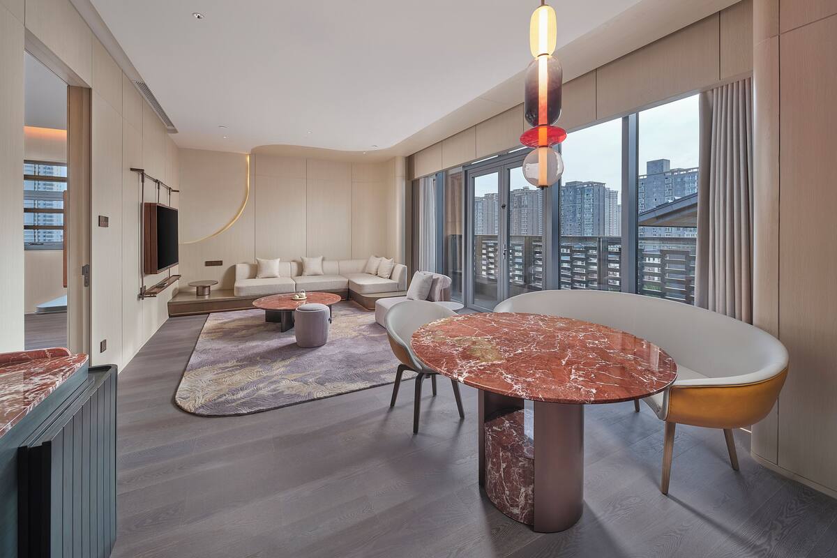 Een moderne woonkamer met een zithoek, een ronde tafel en een groot raam met uitzicht op de stad.