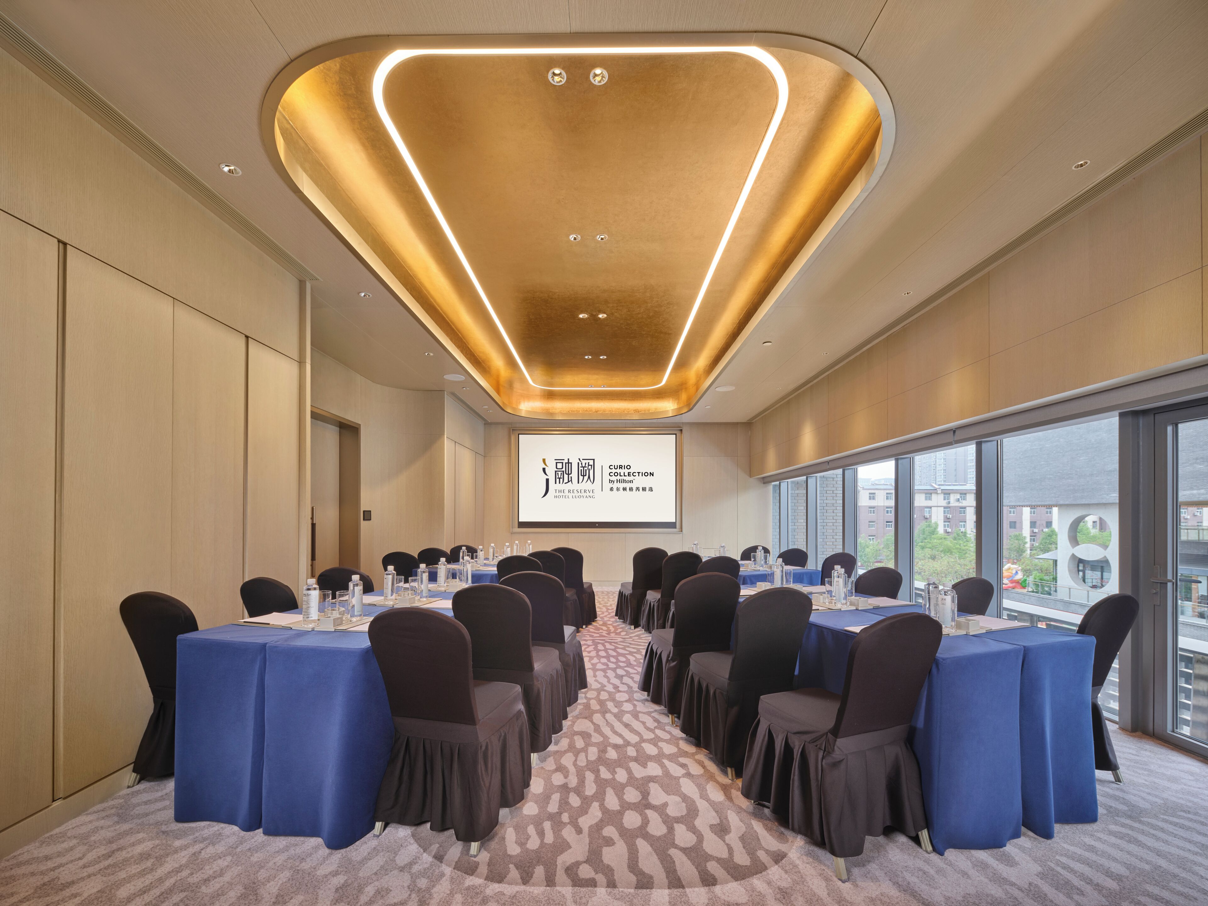 A conference room with a long table, chairs, and a screen displaying text.