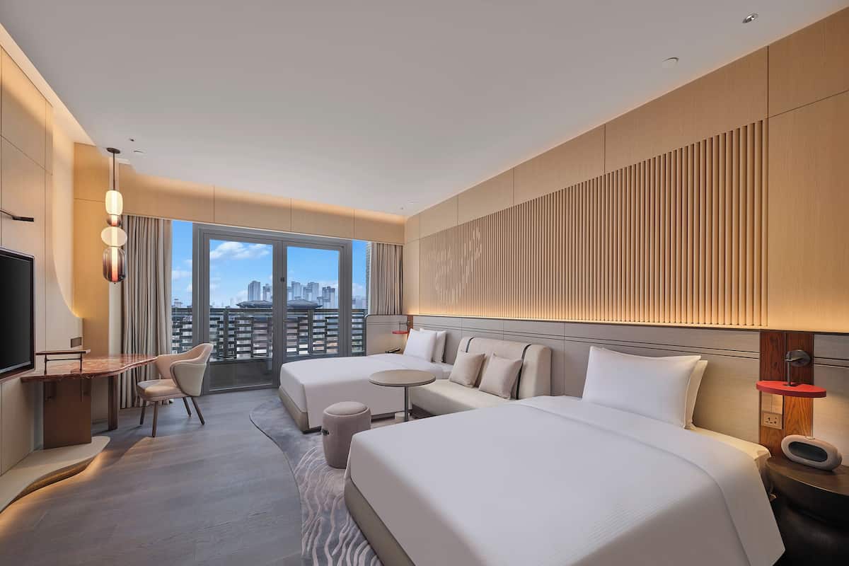 Een moderne hotelkamer met een groot bed, een bureau en een stoel. Grote ramen bieden uitzicht op de stad.