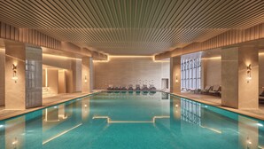 A large indoor swimming pool with a tiled floor, surrounded by lounge chairs and a high ceiling with a ribbed design. - The Reserve Hotel Luoyang, Curio Collection By Hilton (Luoyang)